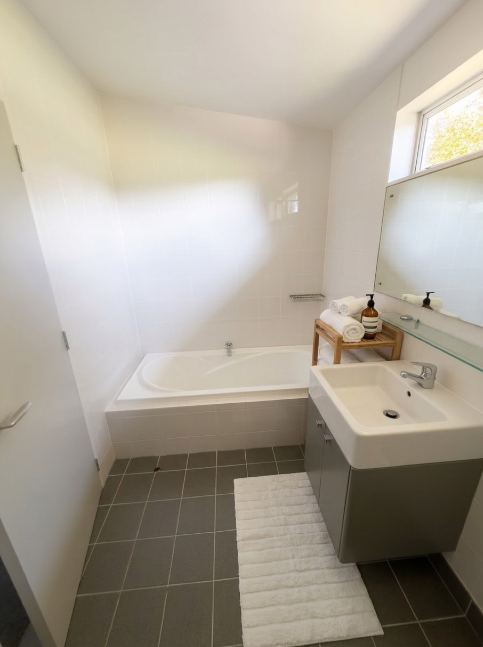 Main bathroom in natural daylight with deep soaking bathtub, square white vessel vanity, plush white towels, and clerestory window