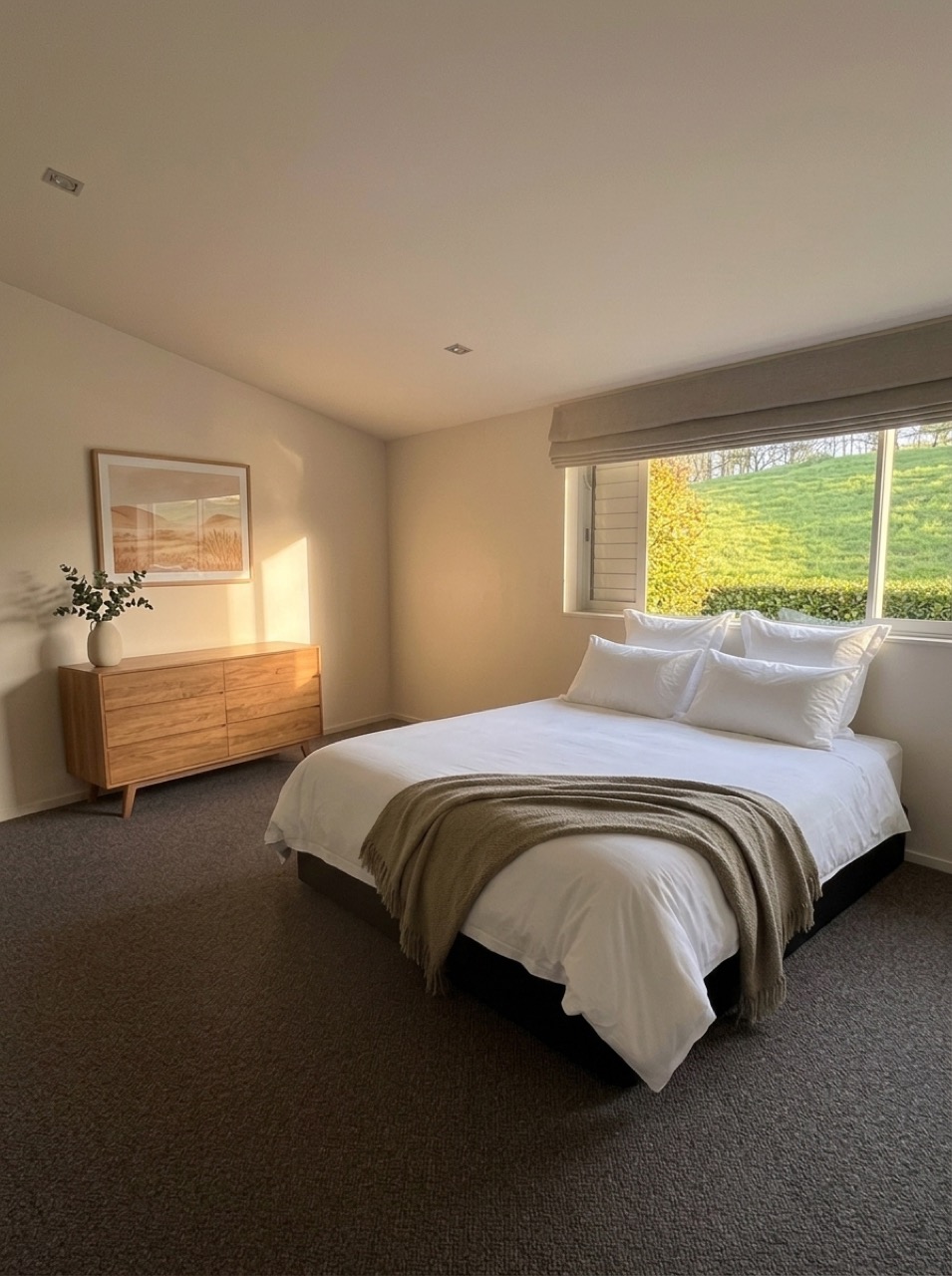 Spacious bedroom in natural daylight with new dark carpet, timber dresser, white hotel linen, and wide window overlooking the green hillside