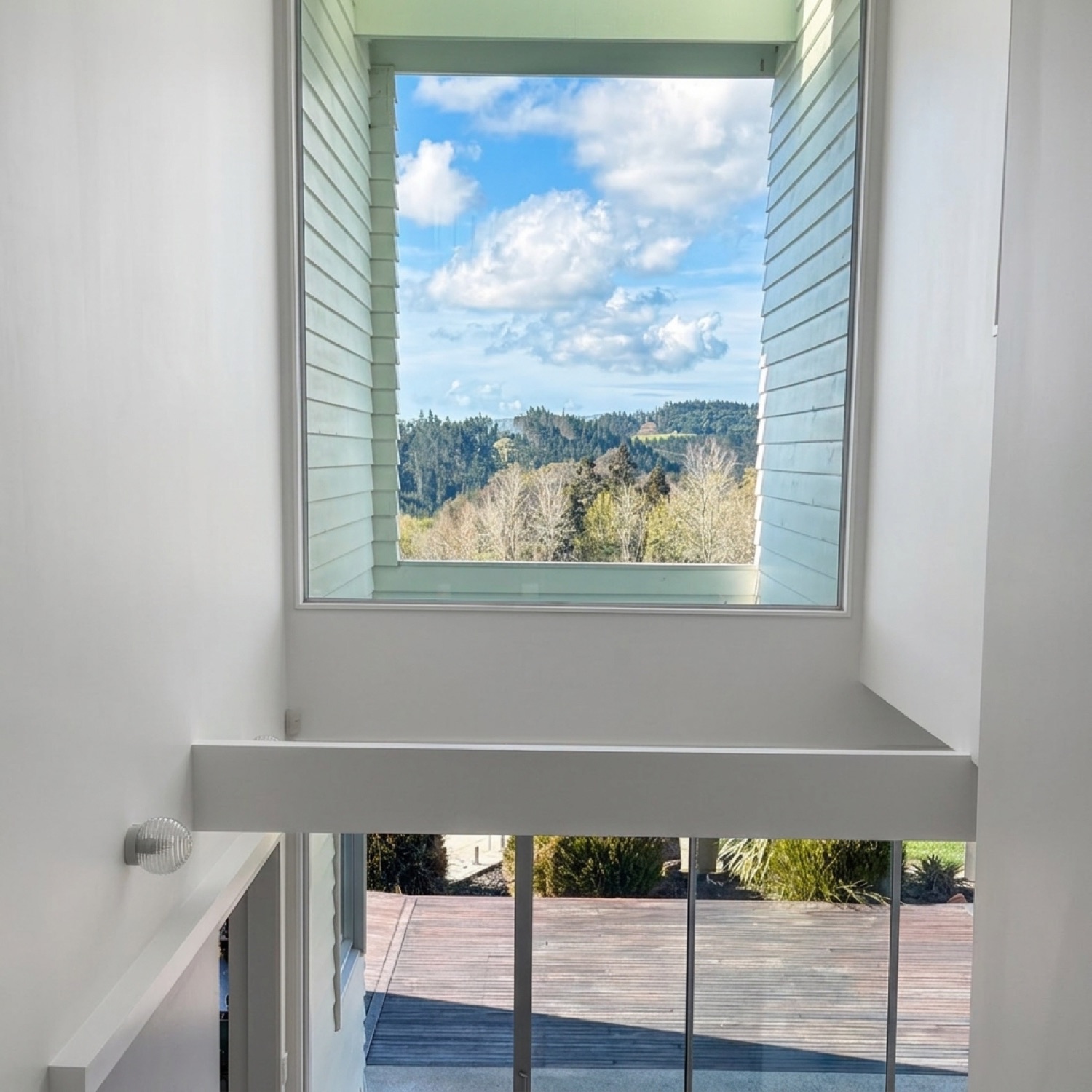 Double-height architectural window framing blue sky and green hills in natural daylight