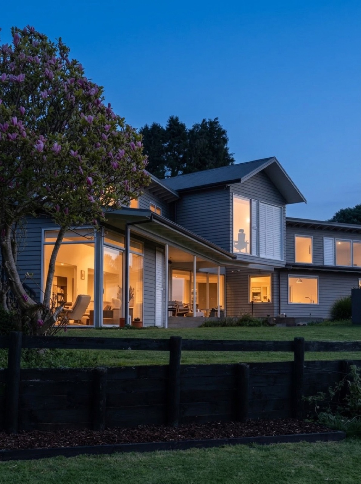 The 393 m² two-level architectural homestead glowing with warm interior window light at dusk