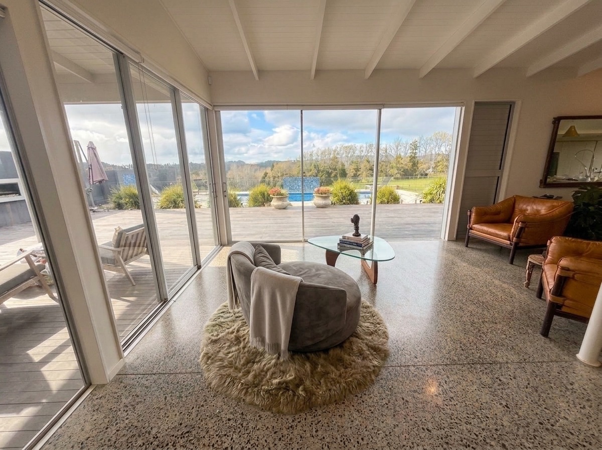 Main living lounge in natural daylight with curved chair, leather armchairs, and floor-to-ceiling sliders to the pool