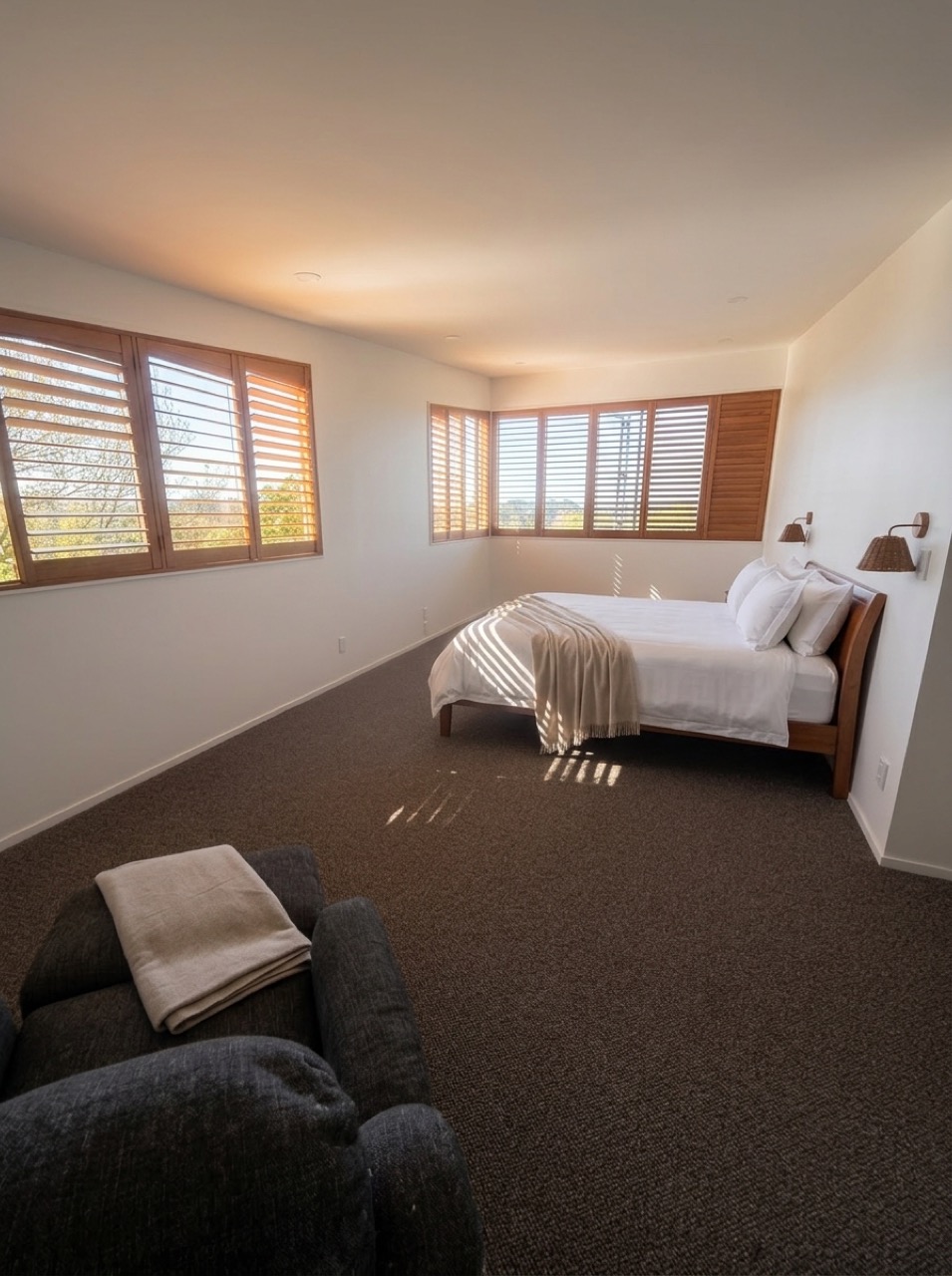 Newly upgraded master bedroom with timber bed frame on the right wall under woven wall sconces, wrap-around cedar plantation shutters, and new dark carpet