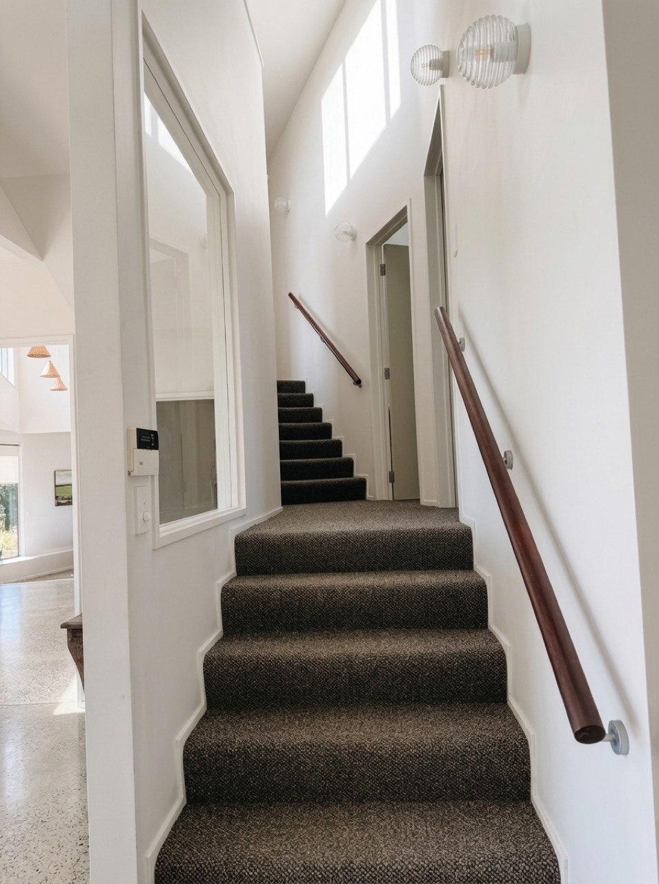 Newly carpeted dark charcoal-brown staircase ascending past ribbed glass wall sconces and a high picture window