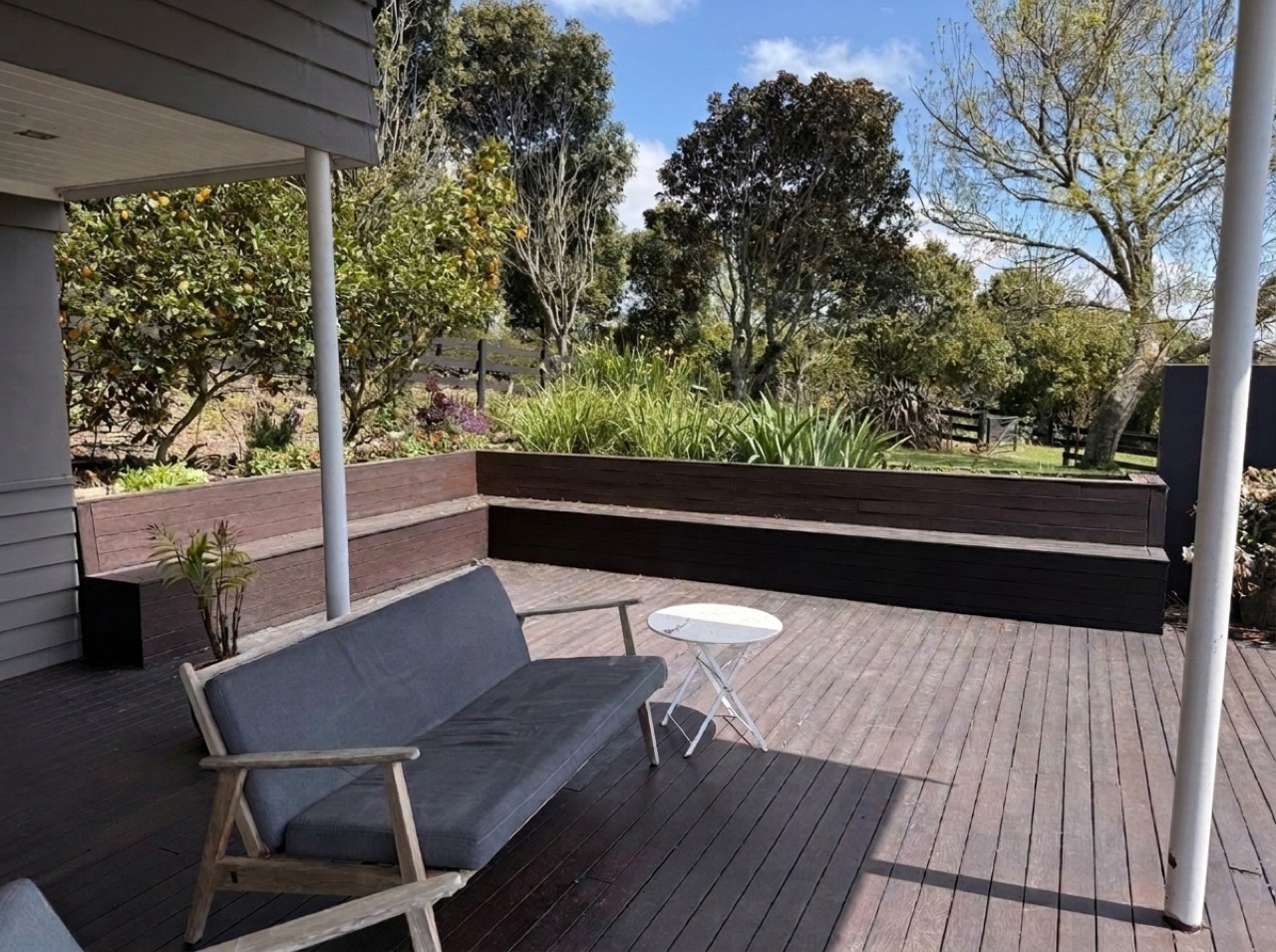 Covered timber veranda with outdoor lounge seating, L-shaped built-in timber bench, fruiting citrus tree, and raised kitchen salad and herb garden